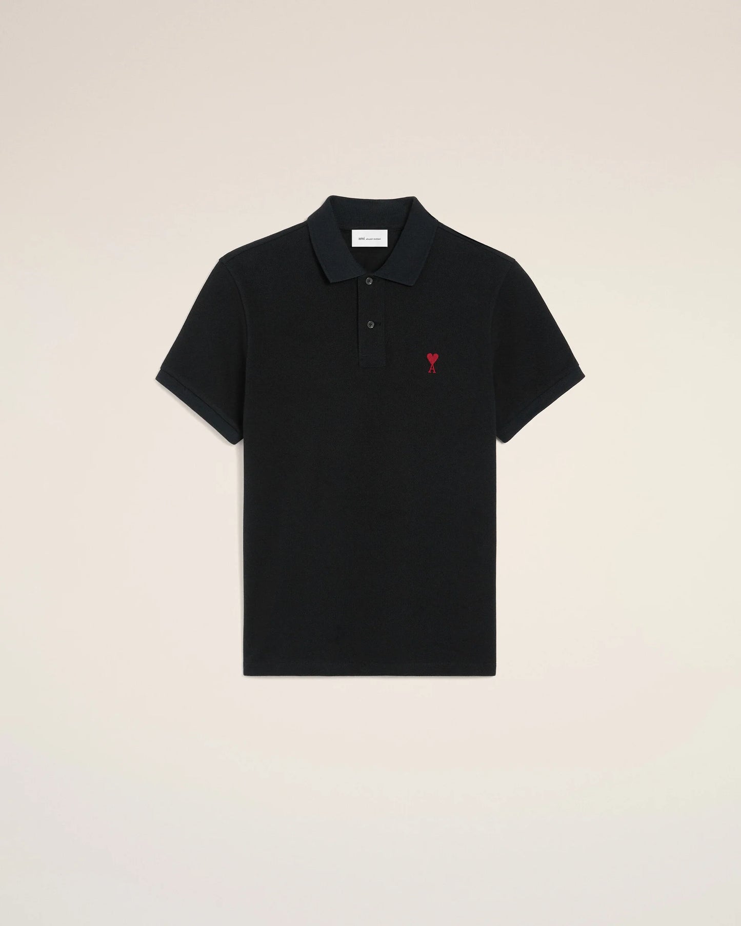 Black polo shirt with a red heart emblem on a beige background ami paris
