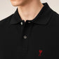 Black polo shirt with a red heart emblem on a beige background ami paris