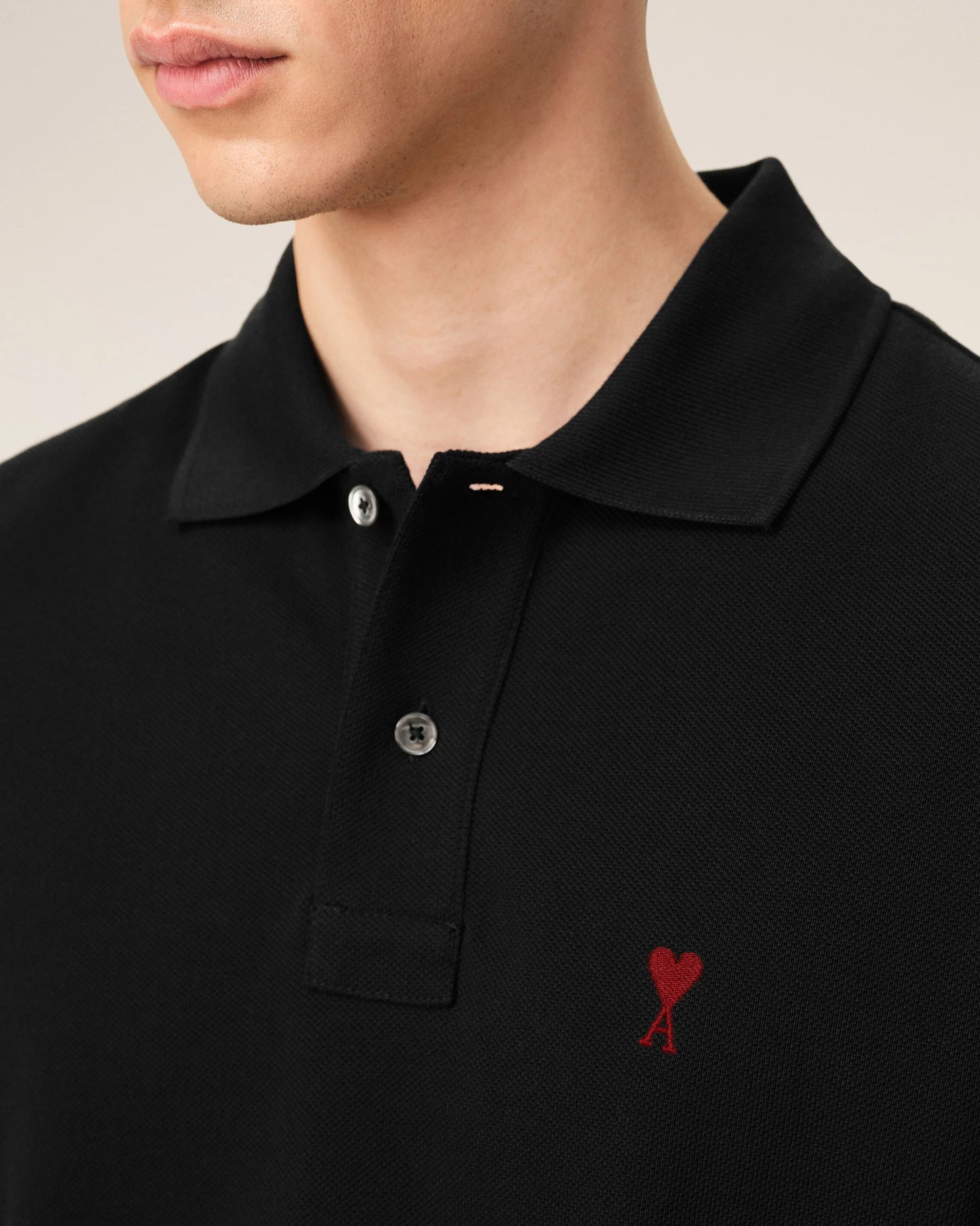 Black polo shirt with a red heart emblem on a beige background ami paris