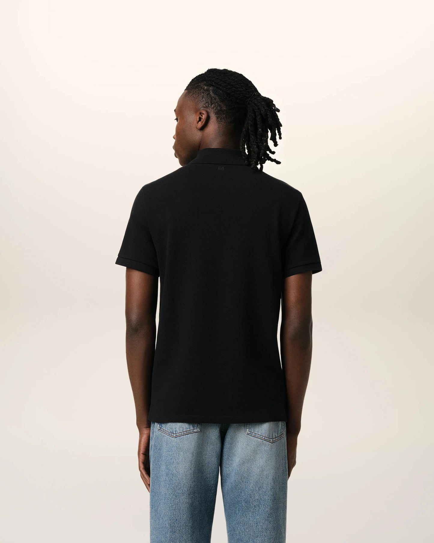 Black polo shirt with a small red logo on a beige background