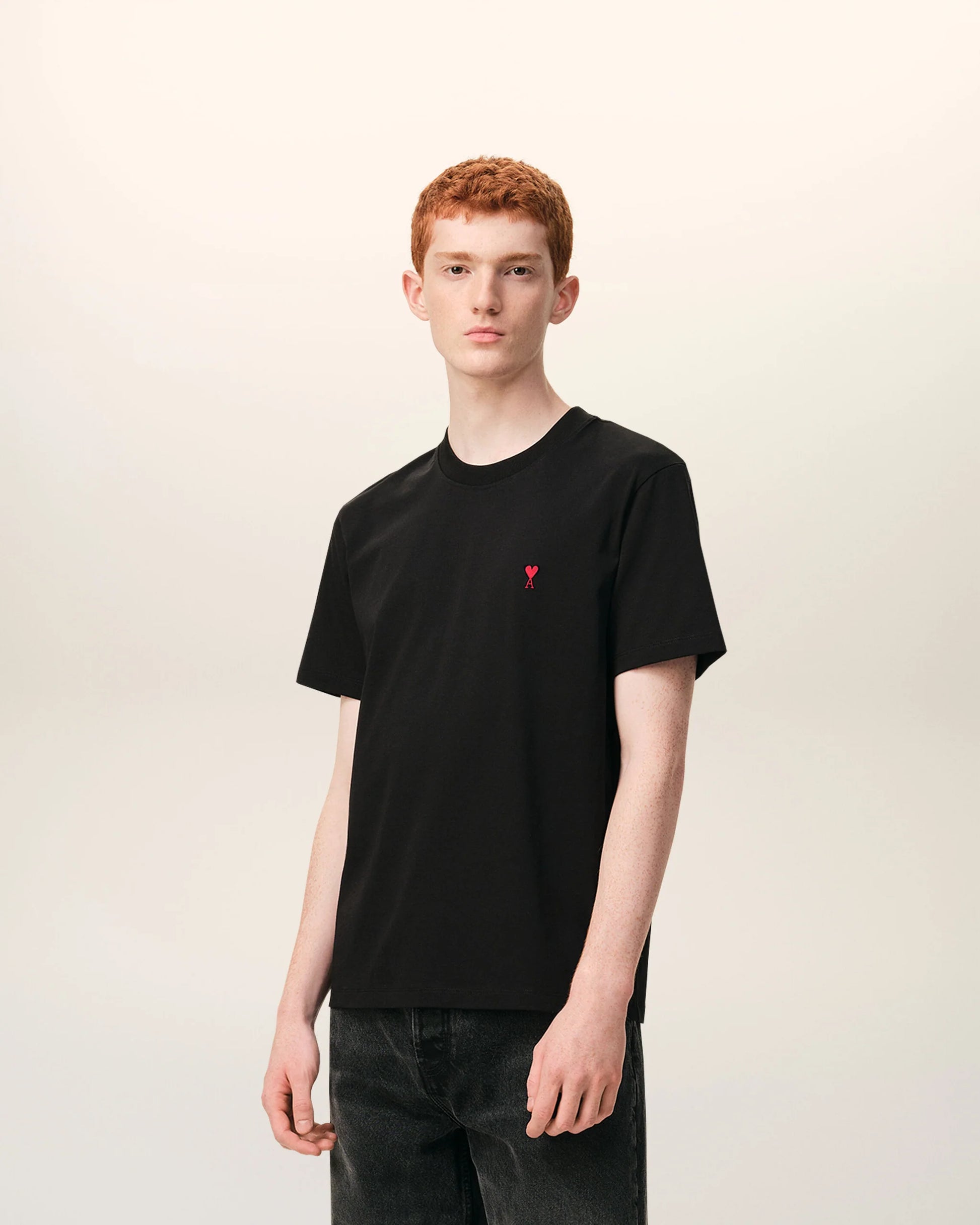 Black t-shirt with a small red logo on a beige background ami paris