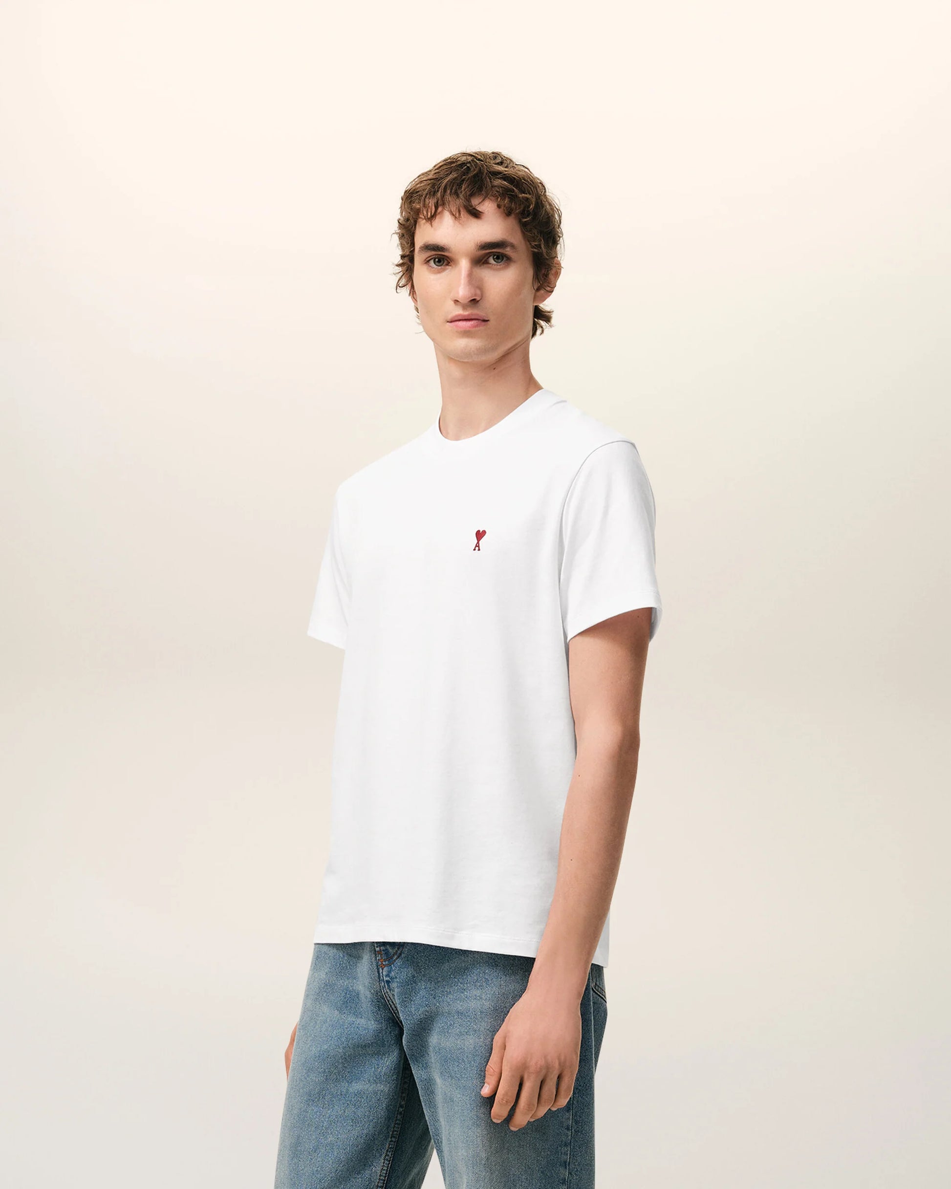 White t-shirt with a small red logo on a beige background Ami paris