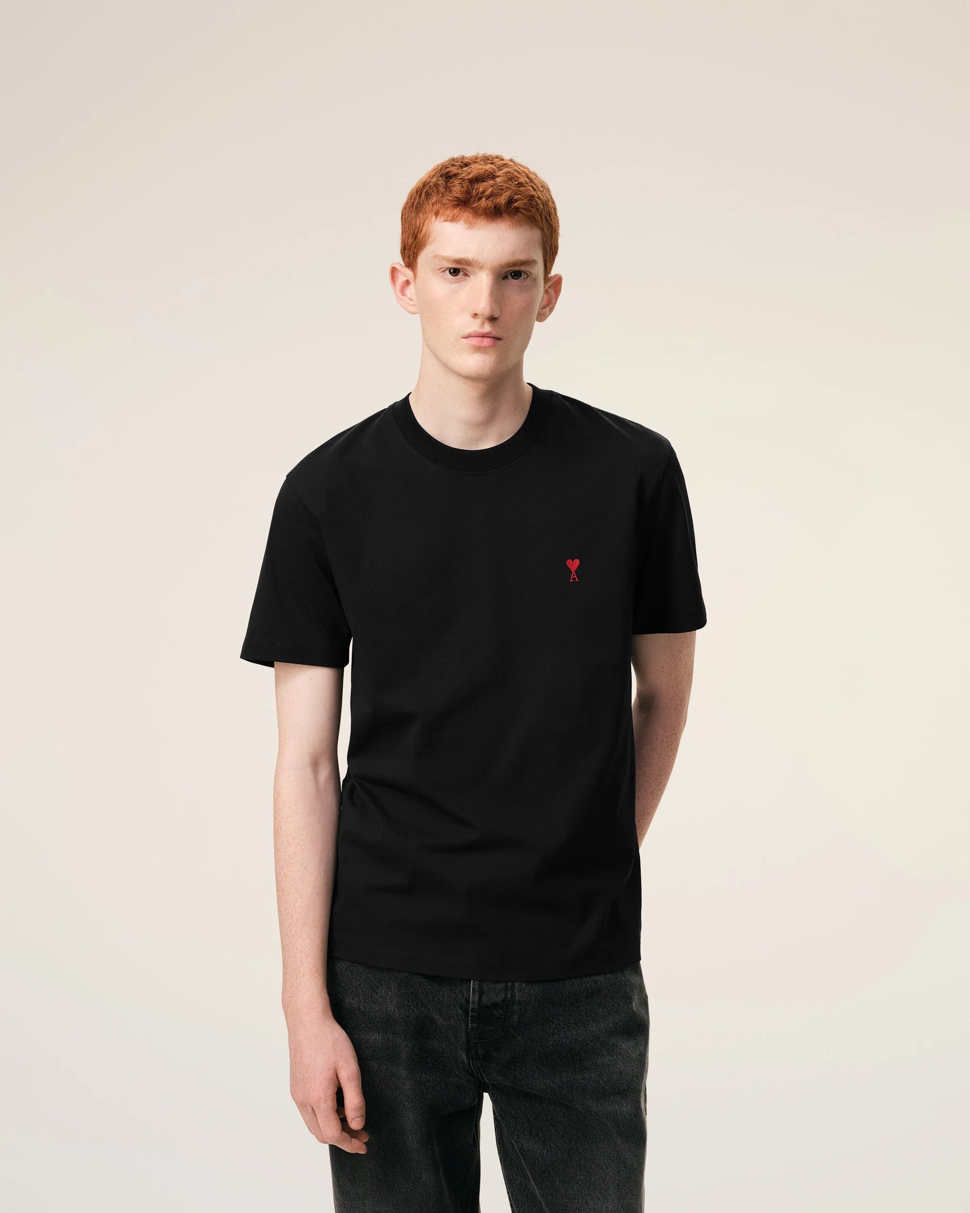 Black t-shirt with a small red logo on a beige background ami paris