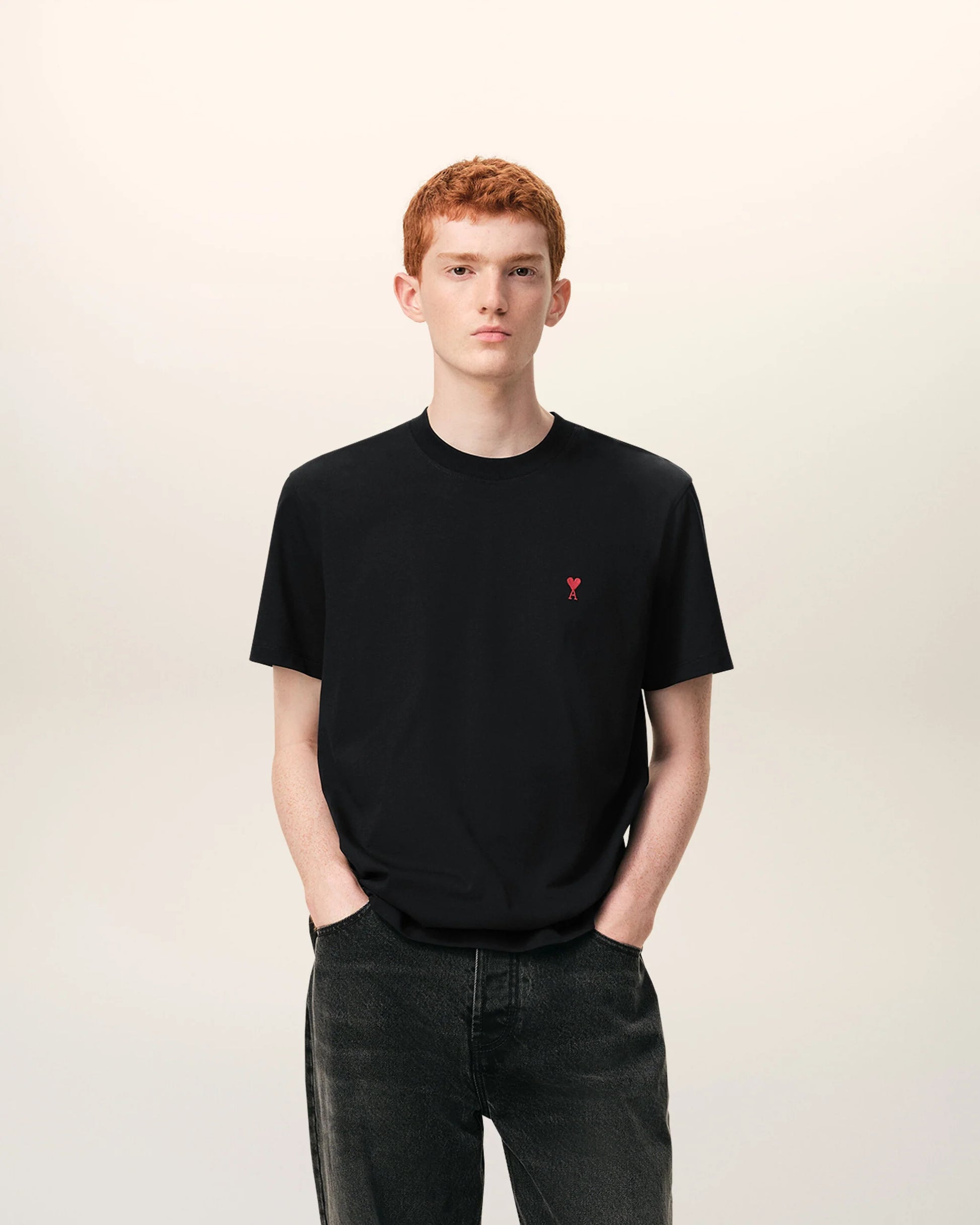 Black t-shirt with a small red logo on a beige background ami paris
