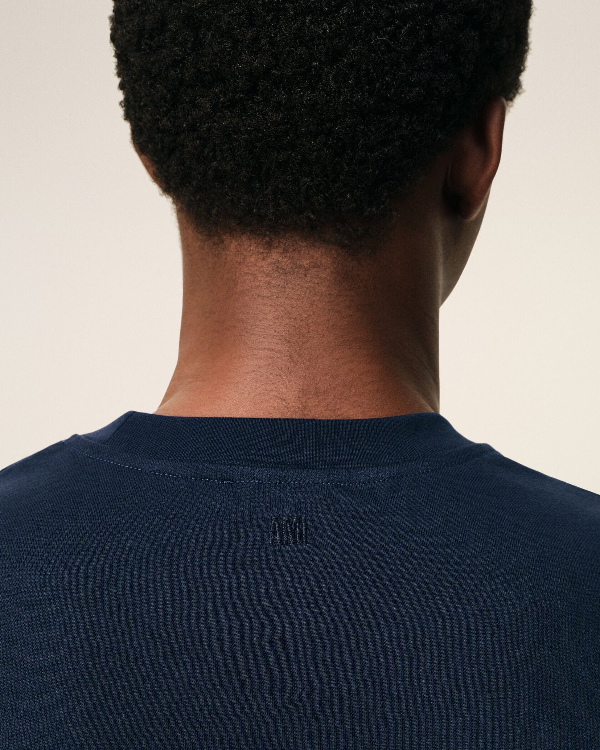 Navy blue t-shirt with a small red logo on a beige background ami paris