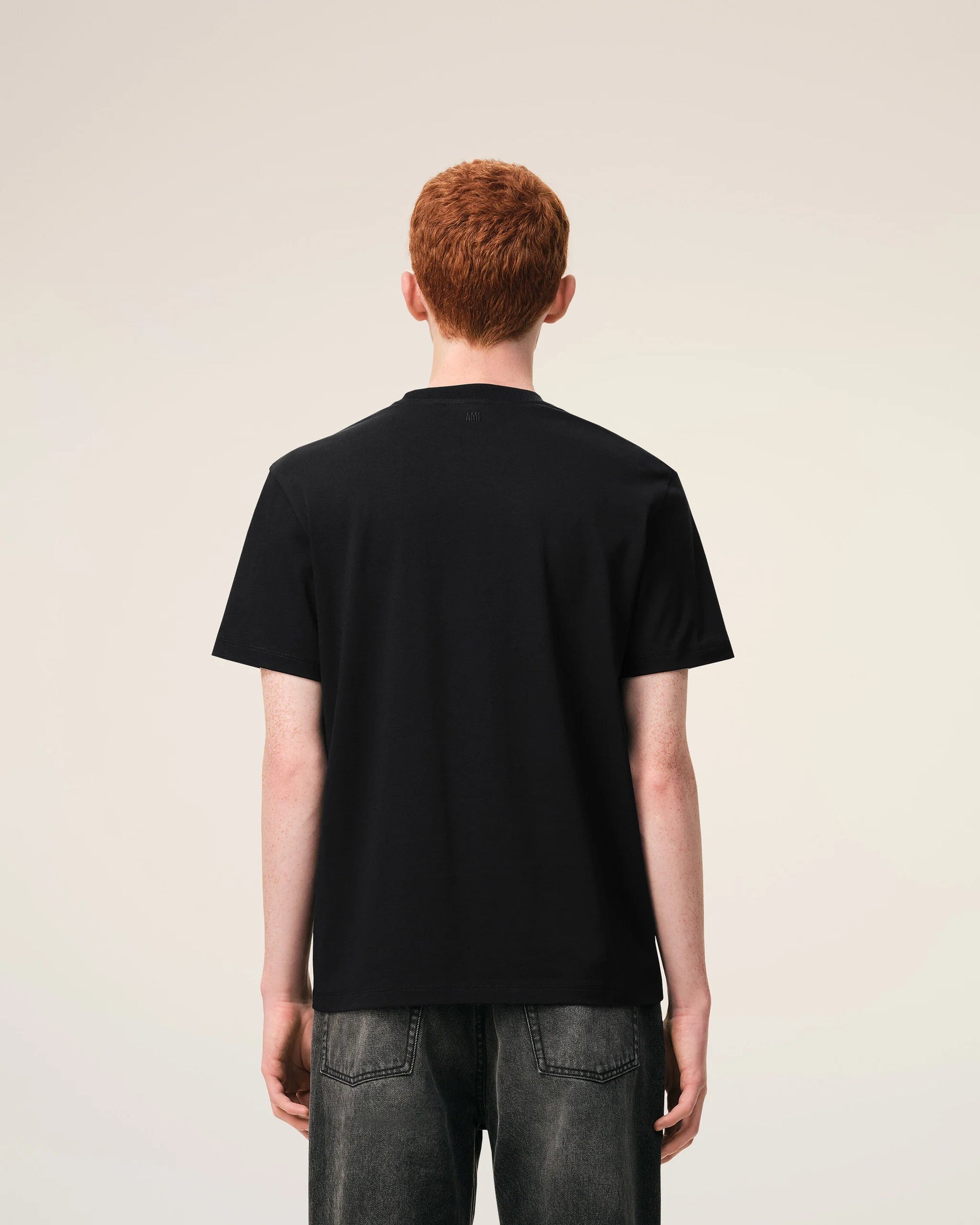 Black t-shirt with a small red logo on a beige background ami paris