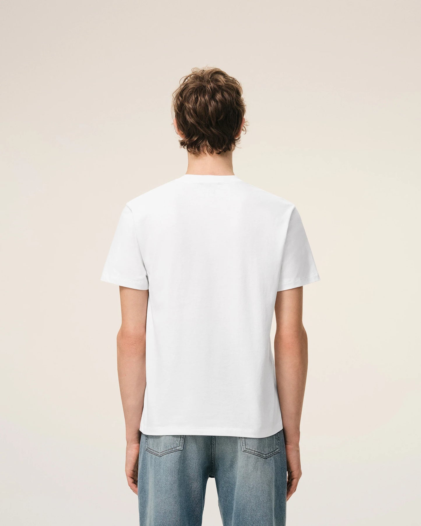 White t-shirt with a small red logo on a beige background Ami paris