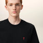 Black t-shirt with a small red logo on a beige background ami paris
