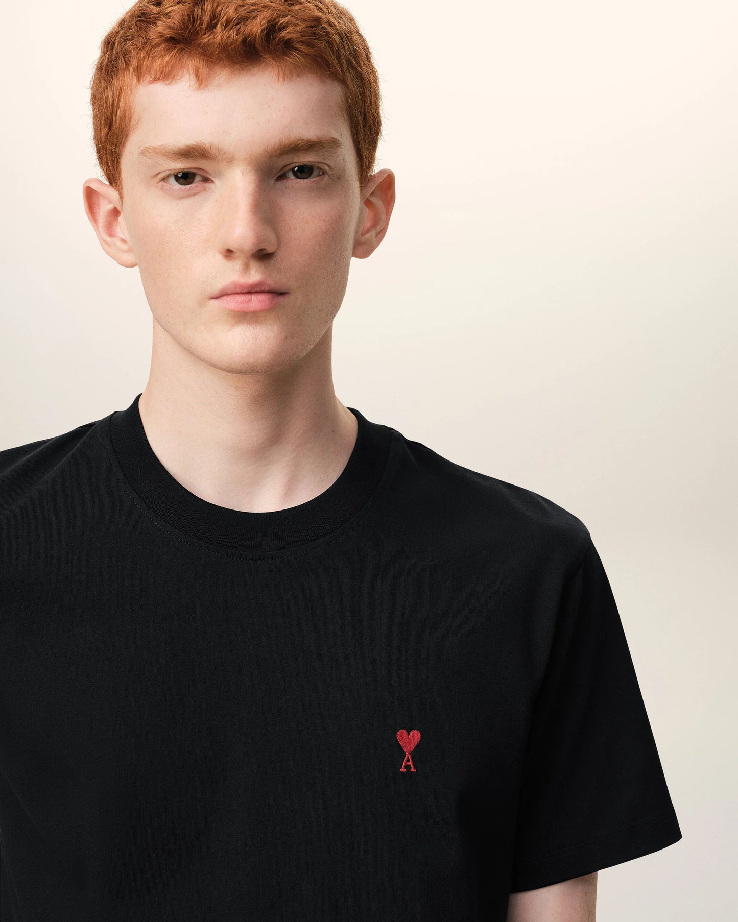 Black t-shirt with a small red logo on a beige background ami paris