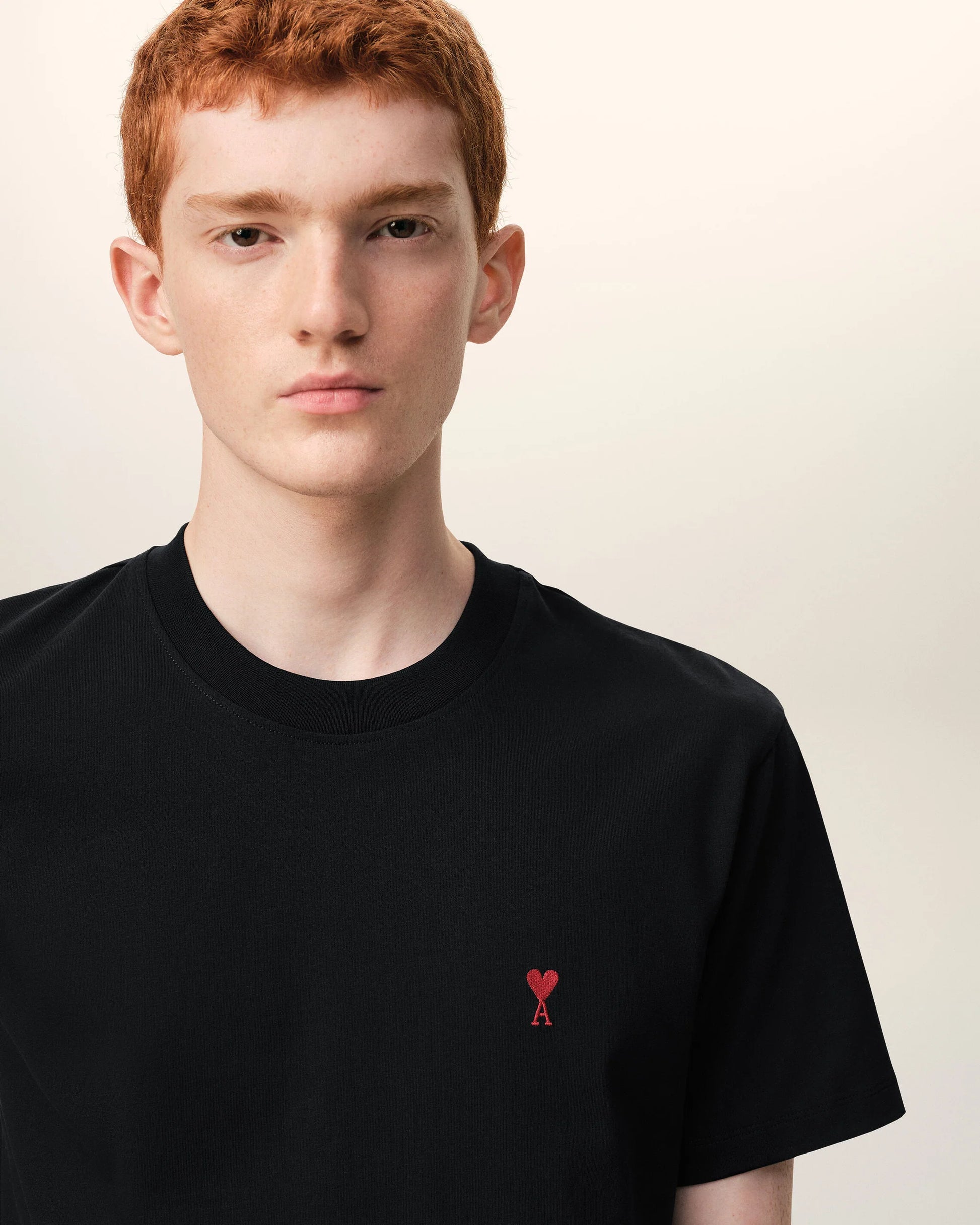 Black t-shirt with a small red logo on a beige background ami paris