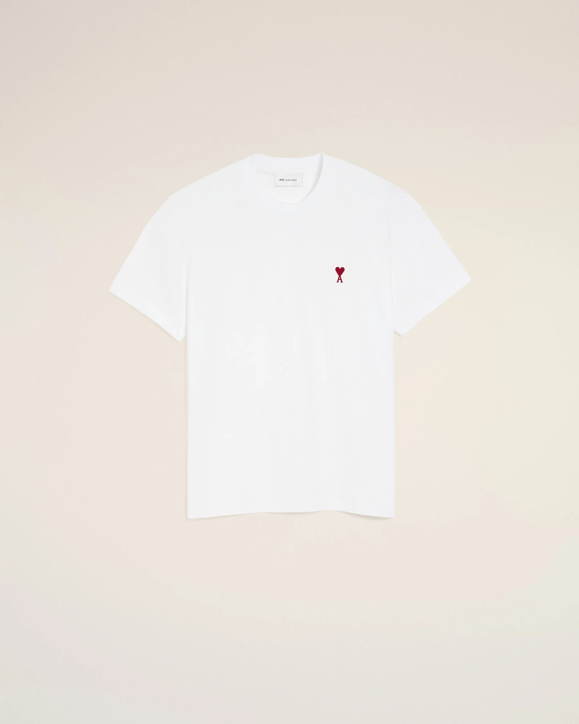 White t-shirt with a small red logo on a beige background Ami paris
