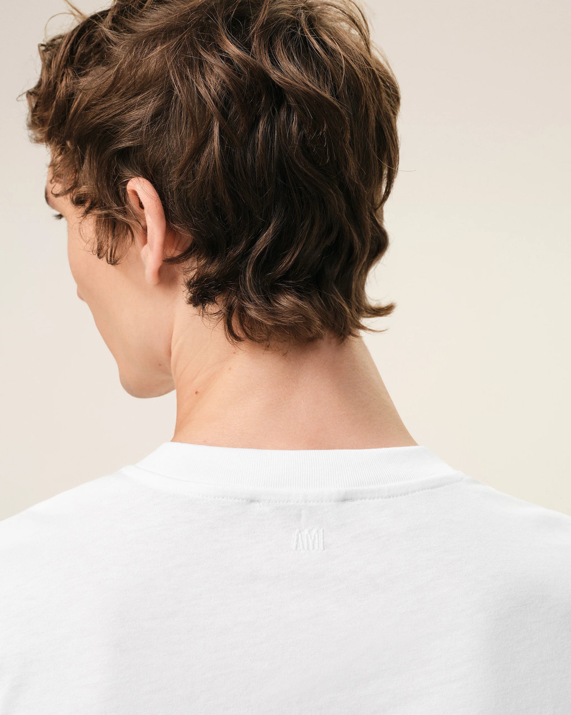 White t-shirt with a small red logo on a beige background Ami paris