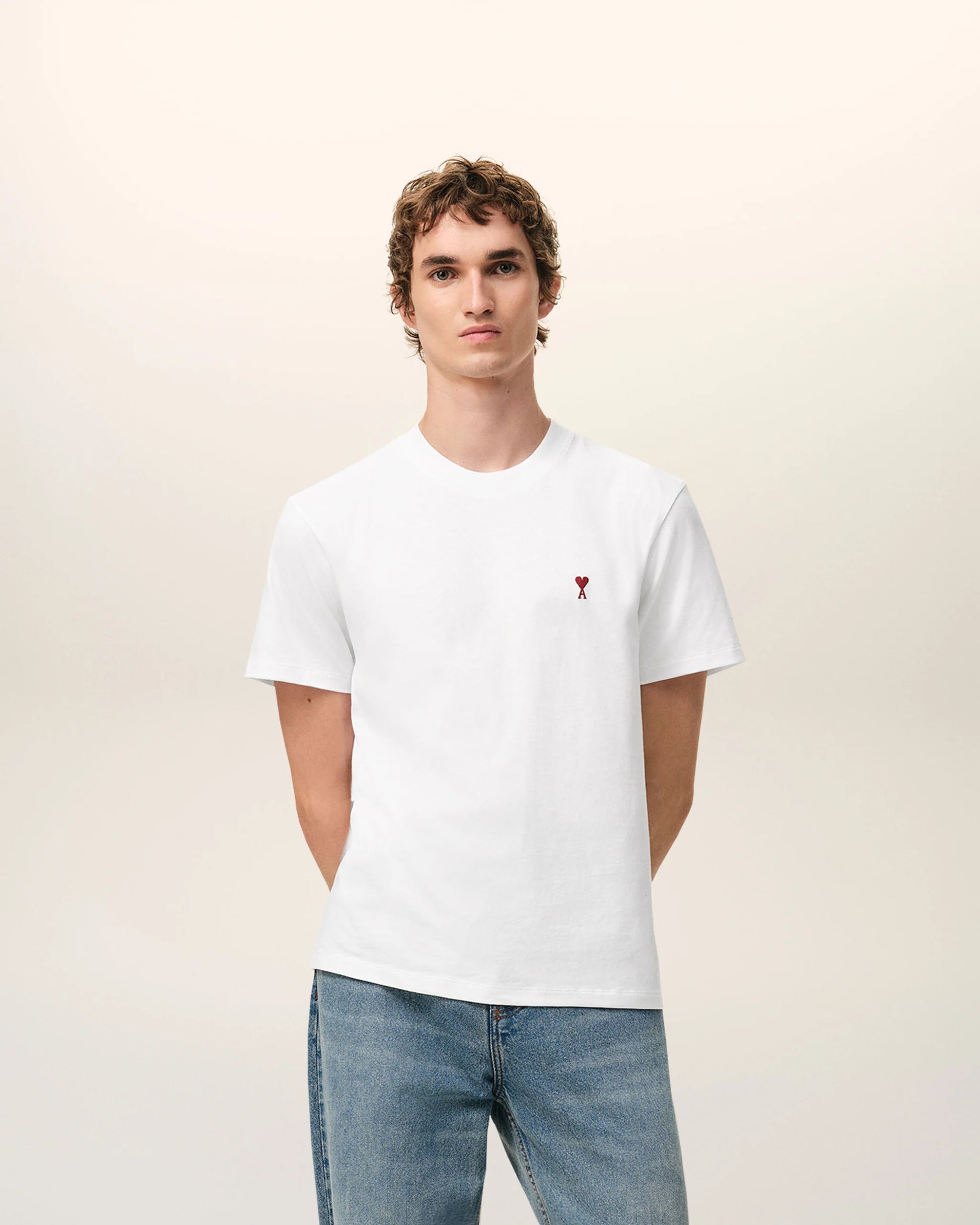 White t-shirt with a small red logo on a beige background Ami paris