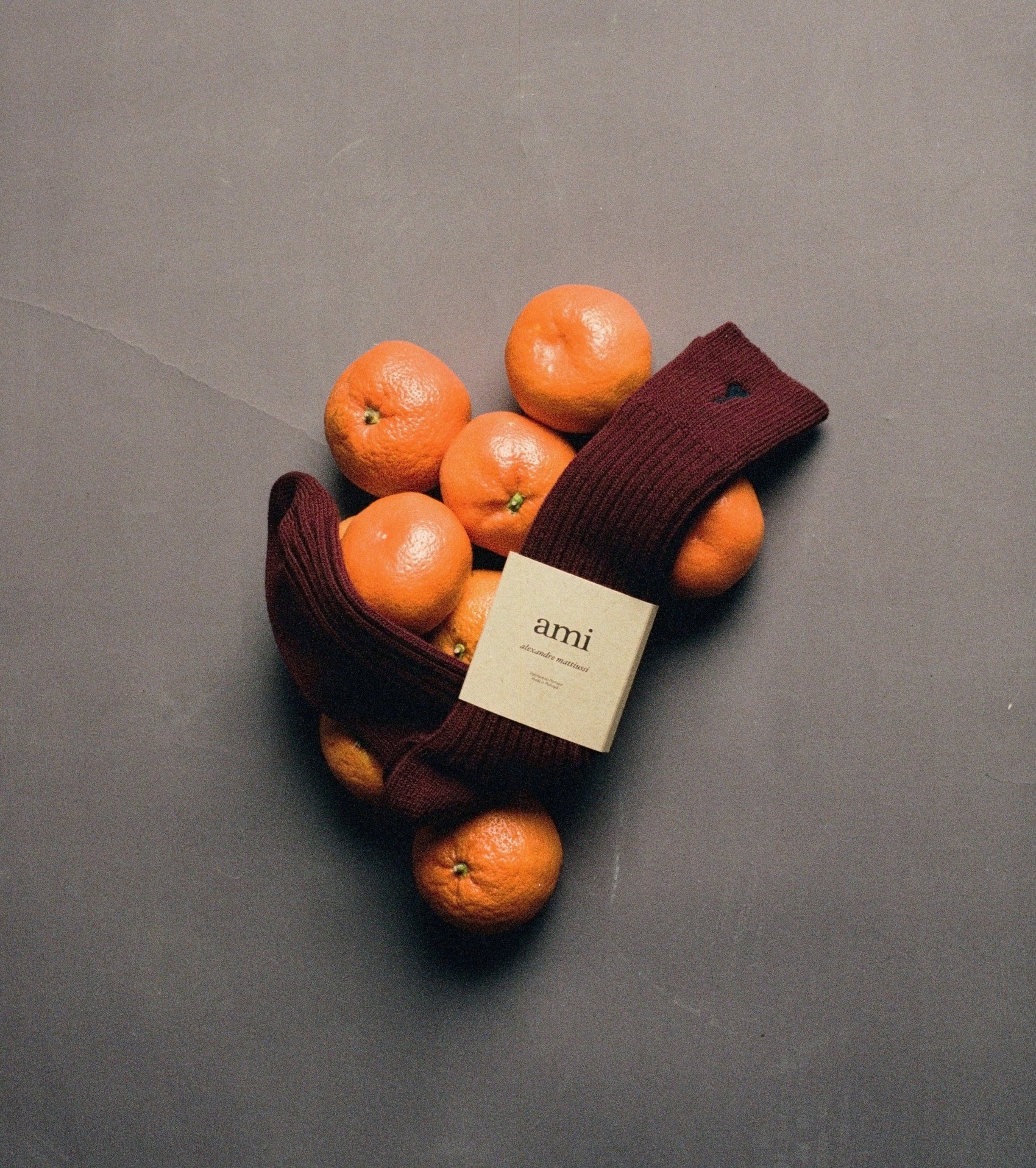 Maroon socks with a label surrounded by oranges on a gray background ami paris