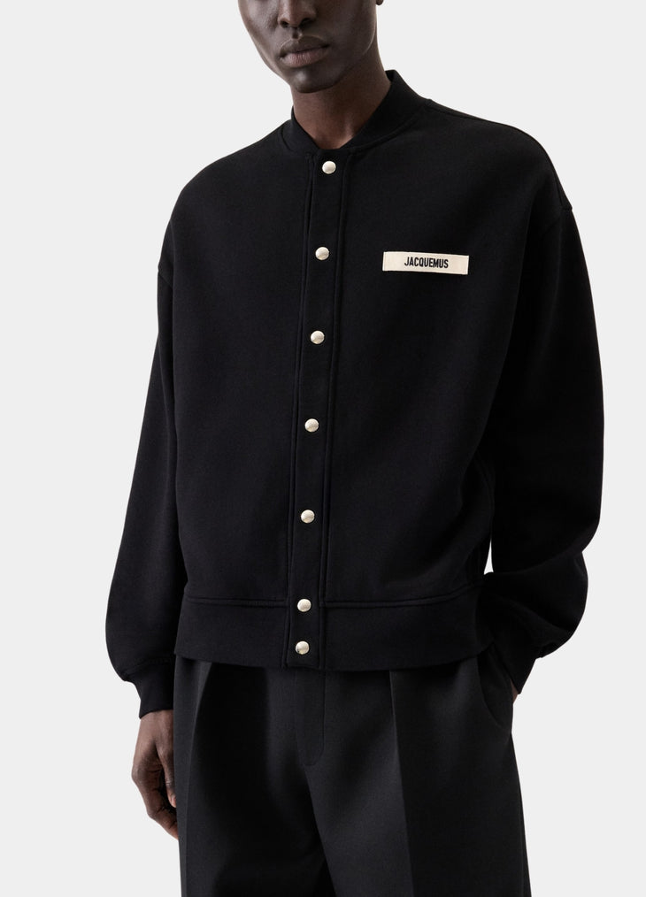 Black varsity jacket with a logo on the chest against a white background