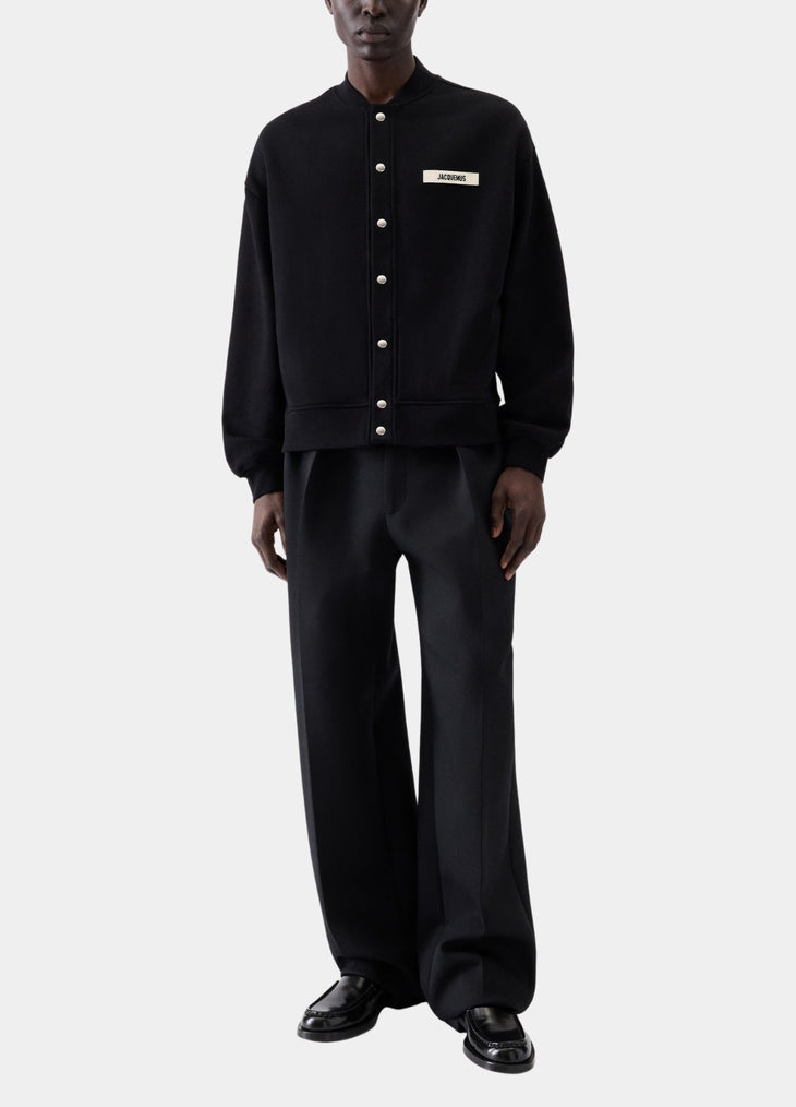 Black varsity jacket with a logo on the chest against a white background