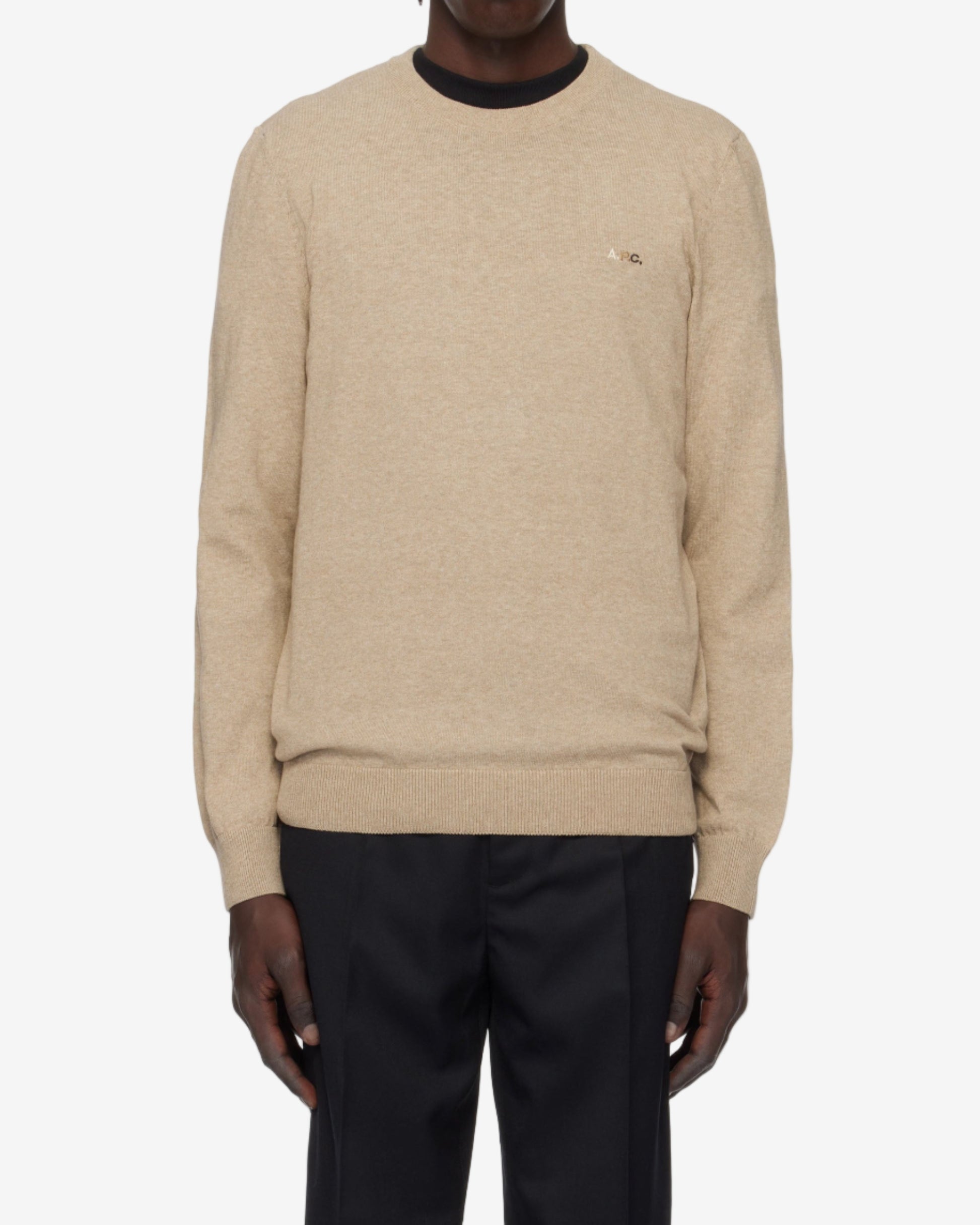 Person wearing a beige sweater and black pants on a white background