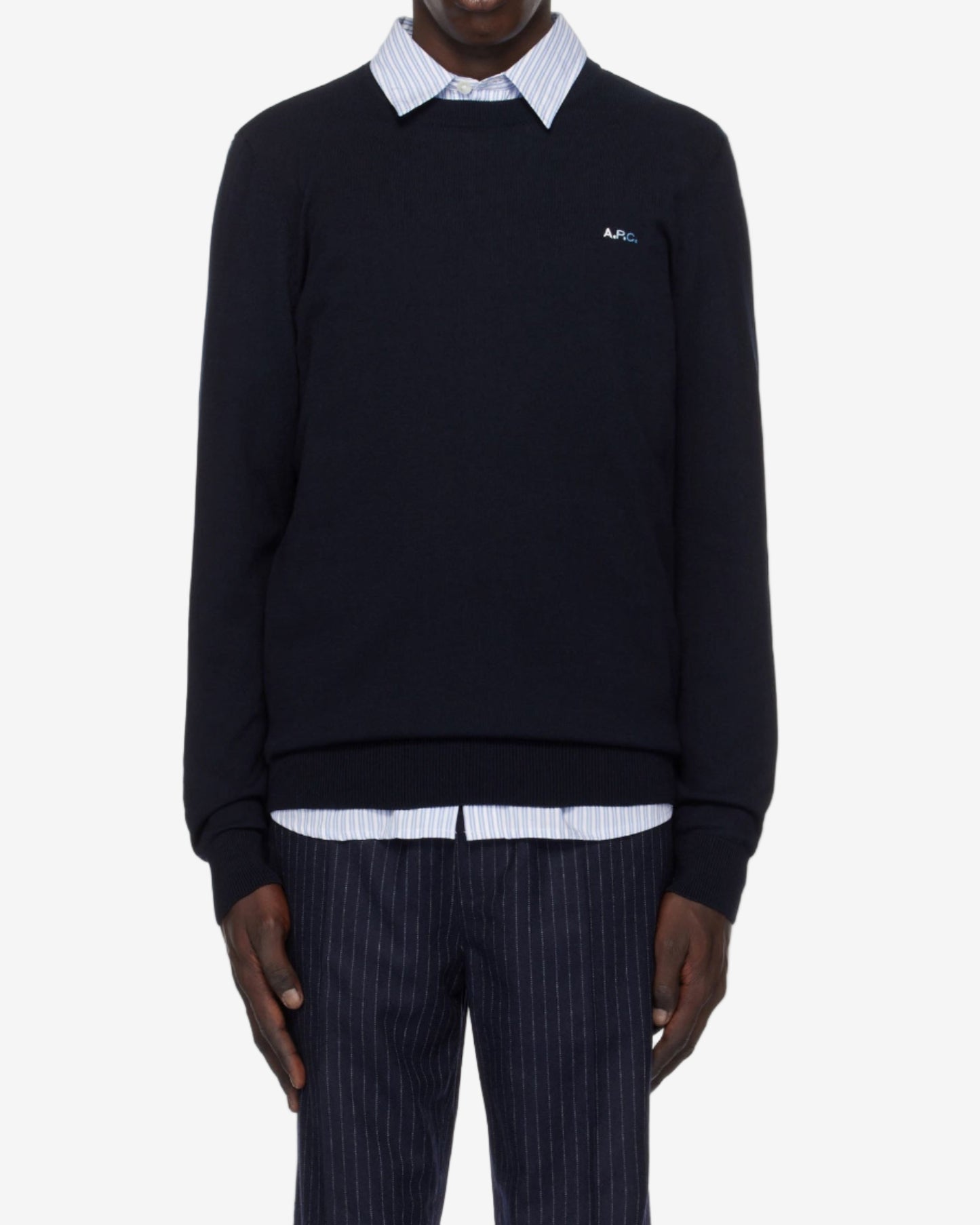 Person wearing a navy sweater with a white collar and pinstripe pants on a white background