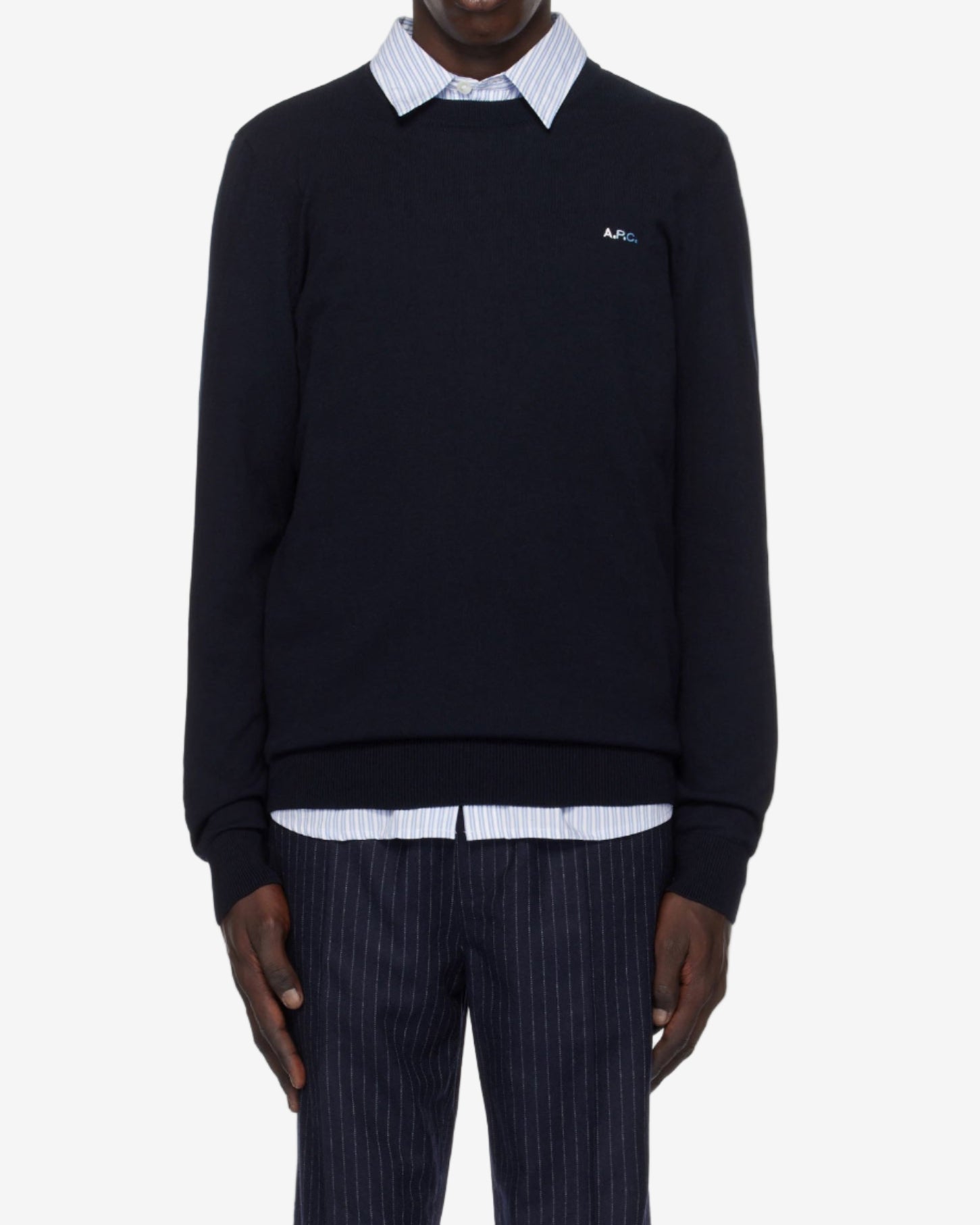 Person wearing a navy sweater with a white collar and pinstripe pants on a white background