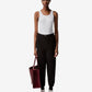 Person wearing a white tank top, black pants, and white sneakers, holding a red bag on a white background