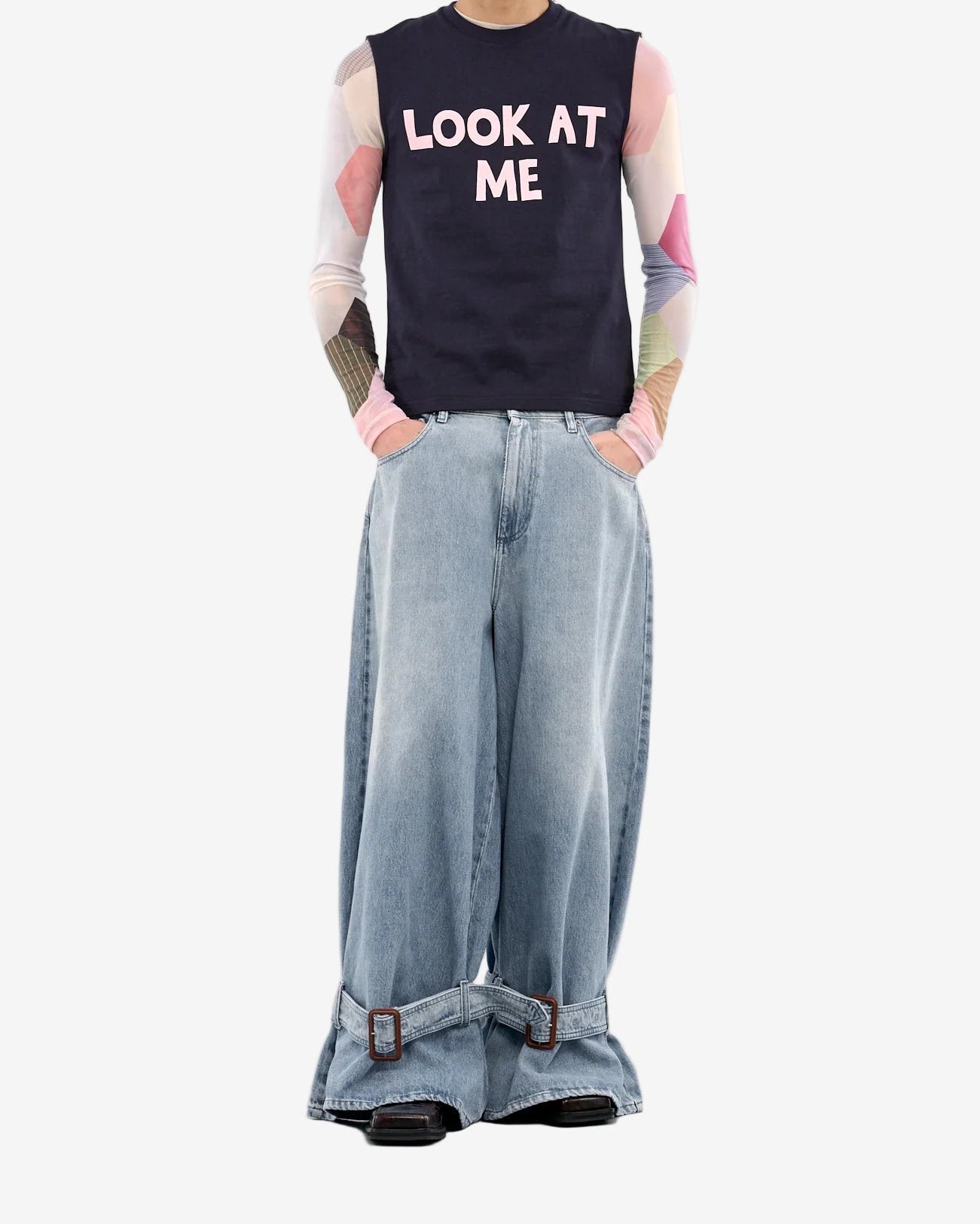 Person wearing a sleeveless shirt with 'LOOK AT ME' text and wide-leg jeans on a white background