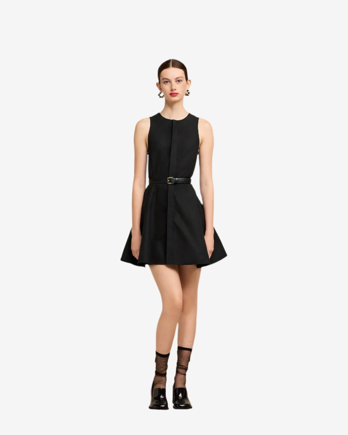 Woman wearing a black sleeveless dress with a belt against a plain background