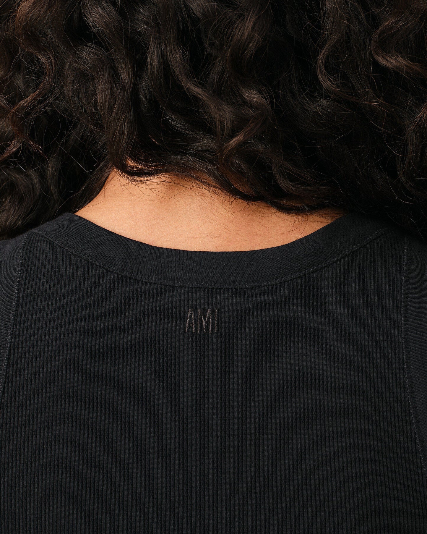 Black tank top with a small white logo on a beige background