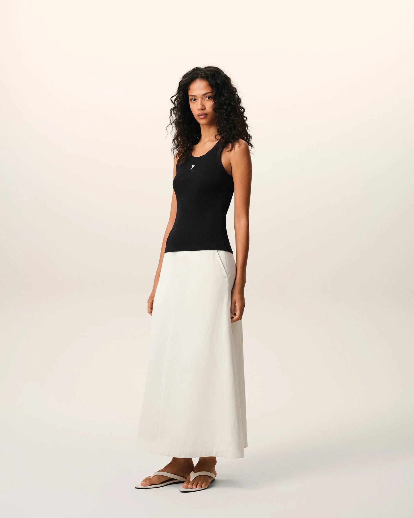 Black tank top with a small white logo on a beige background