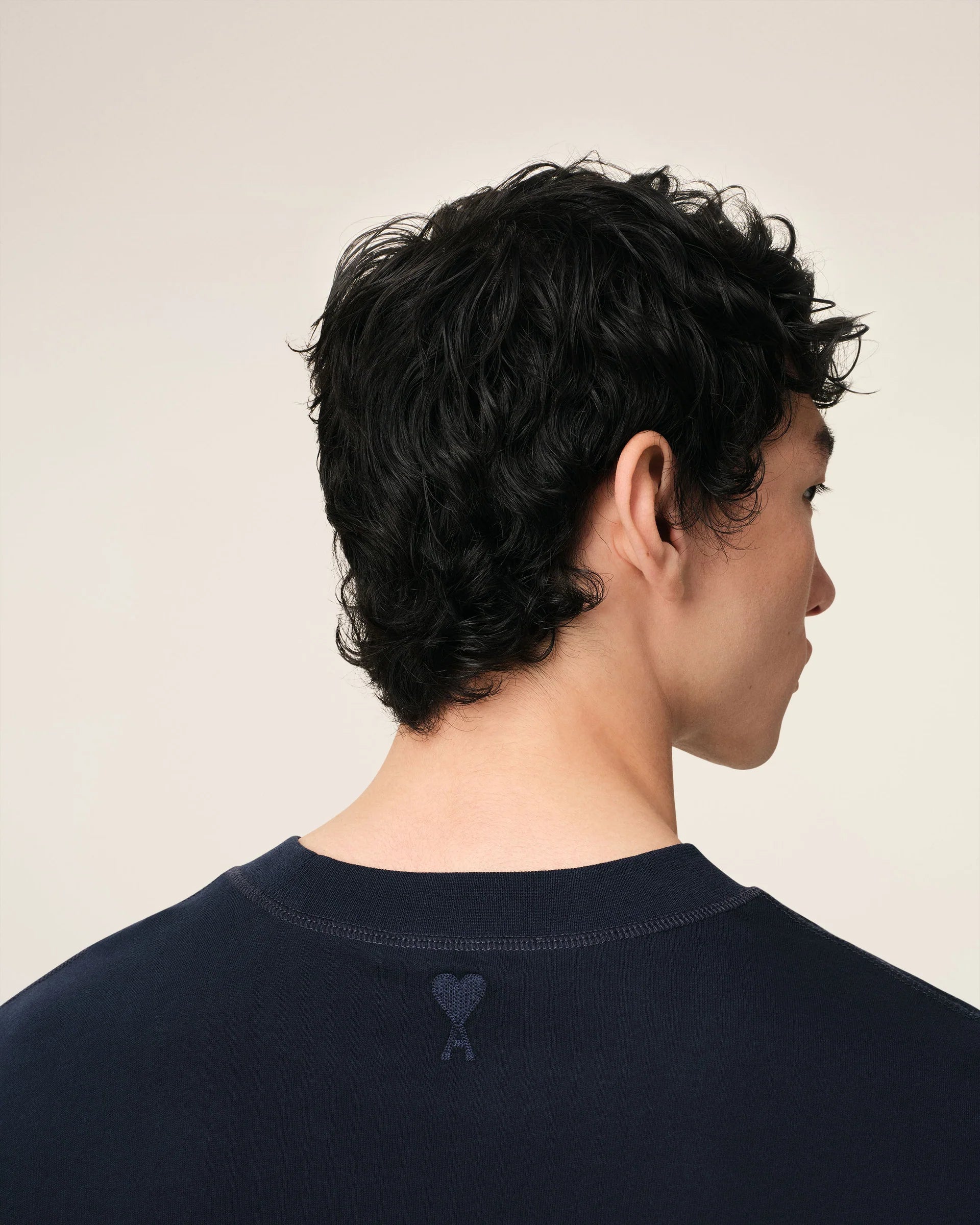 Navy blue t-shirt with 'ami' logo on a beige background ami paris