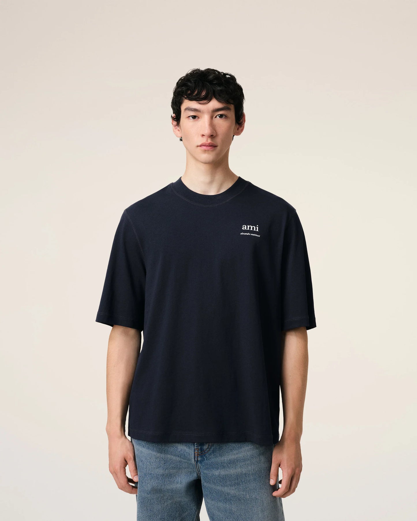 Navy blue t-shirt with 'ami' logo on a beige background ami paris