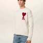 Person wearing a white sweater with a red heart and letter 'A' design, paired with blue jeans on a light background.