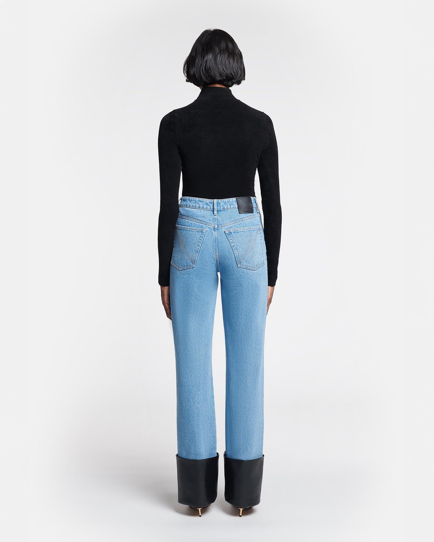 Person wearing light blue jeans with black cuffs on a white background