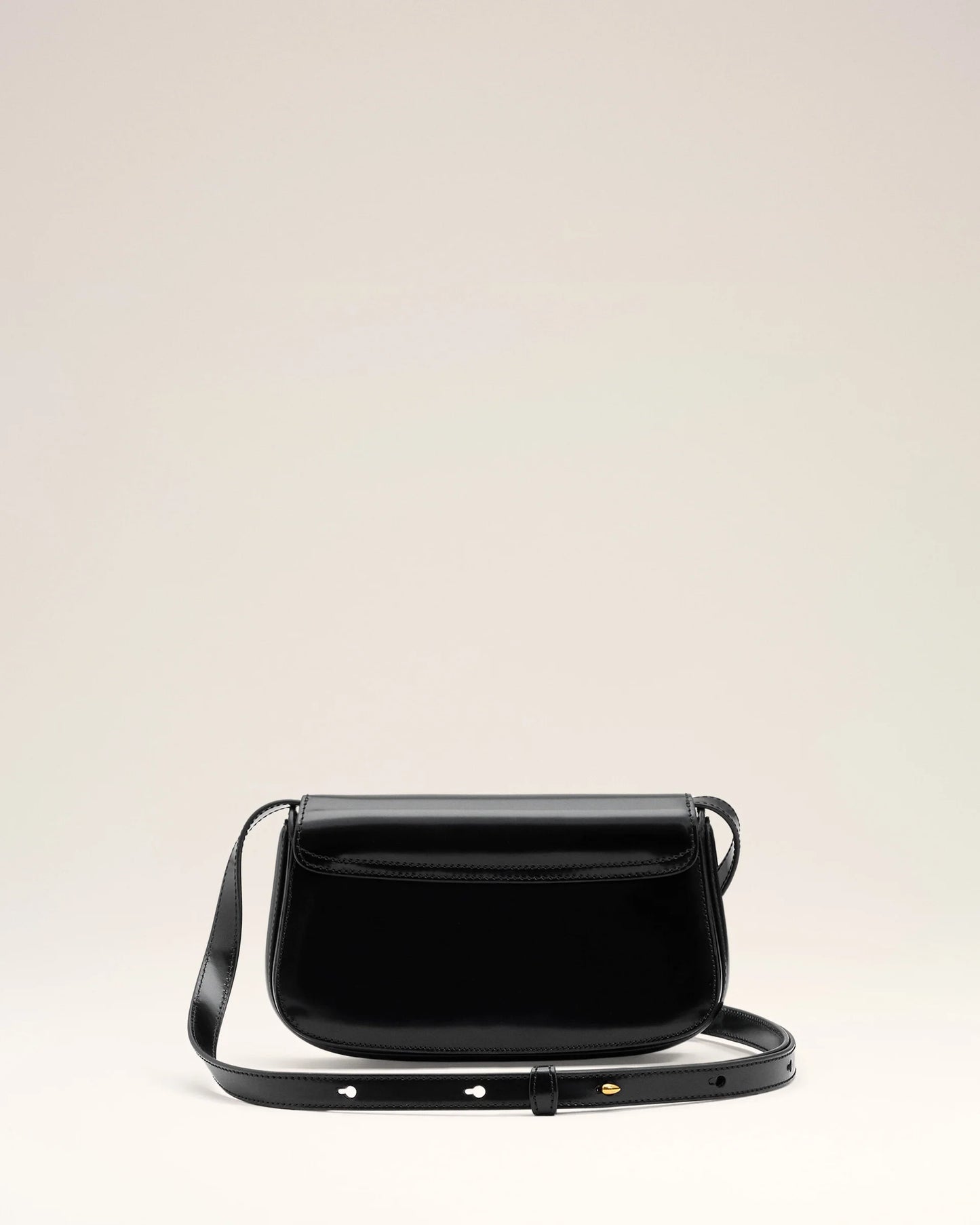 Person holding a black handbag with a gold emblem against a neutral background ami paris