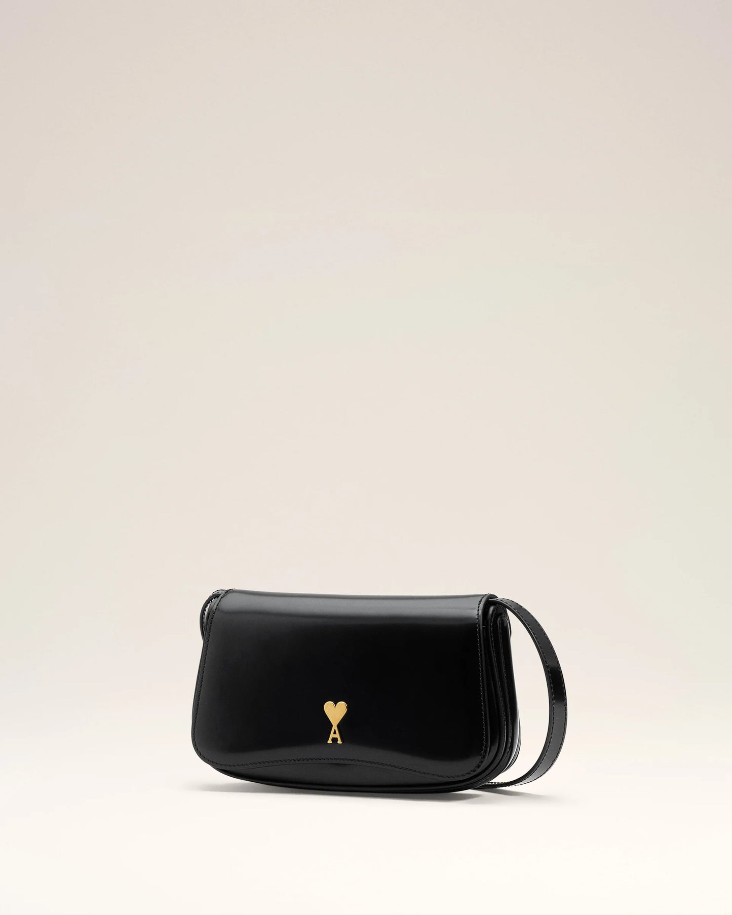 Person holding a black handbag with a gold emblem against a neutral background ami paris