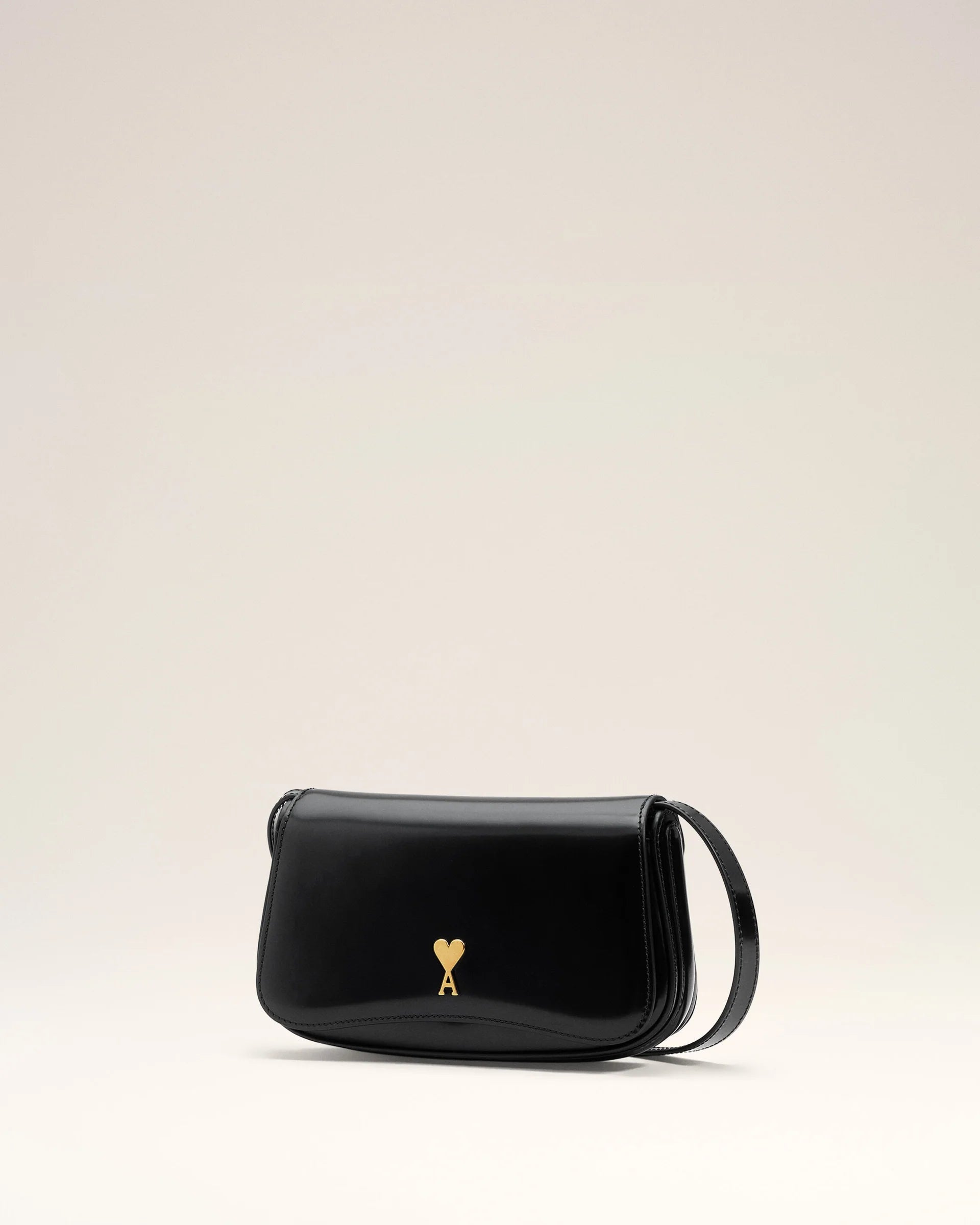 Person holding a black handbag with a gold emblem against a neutral background ami paris
