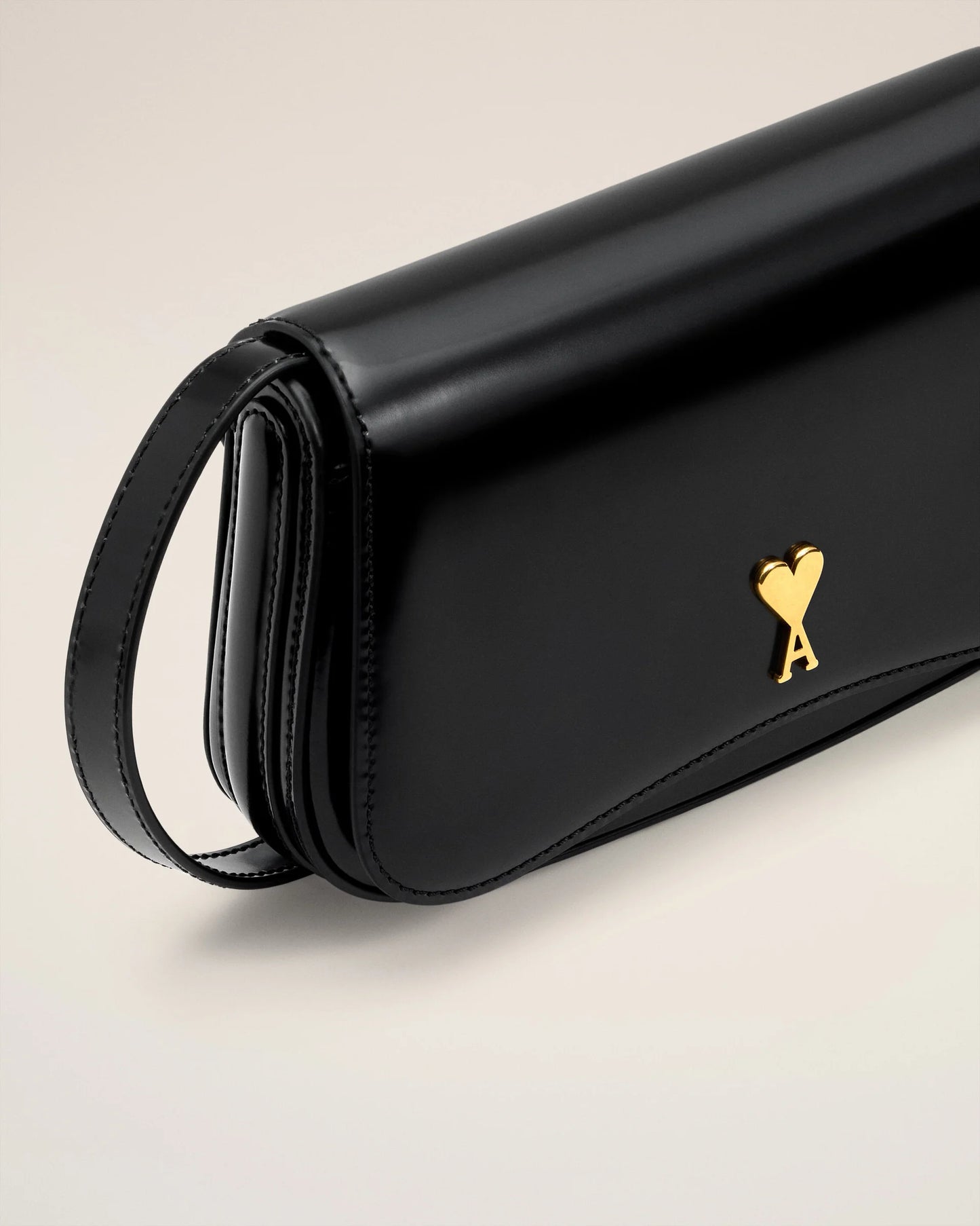 Person holding a black handbag with a gold emblem against a neutral background ami paris