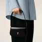 Person holding a black handbag with a gold emblem against a neutral background ami paris