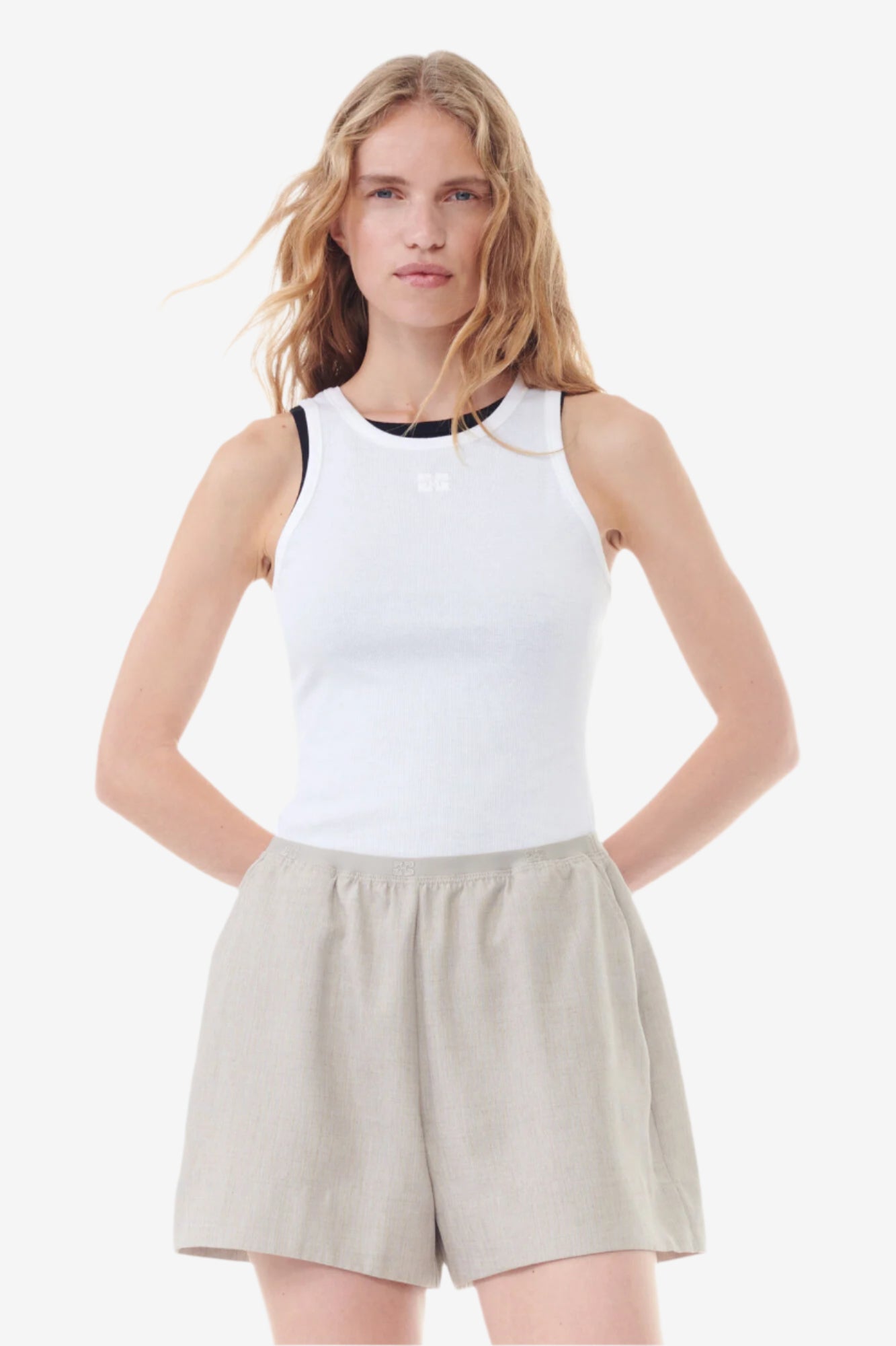 Woman wearing a white sleeveless top and beige shorts on a white background