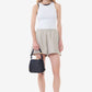 Woman wearing a white sleeveless top and beige shorts, holding a black handbag on a white background