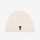 Beige knit beanie with a black heart emblem on a light gray background