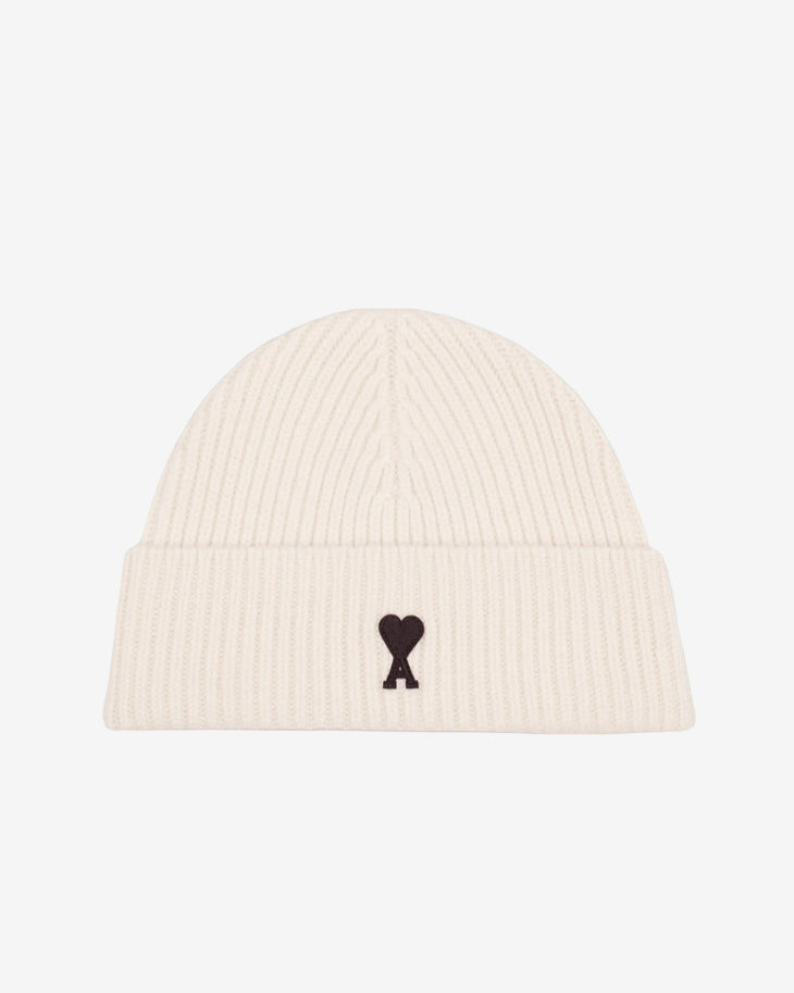 Beige knit beanie with a black heart emblem on a light gray background