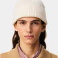 Beige knit beanie with a black heart emblem on a light gray background