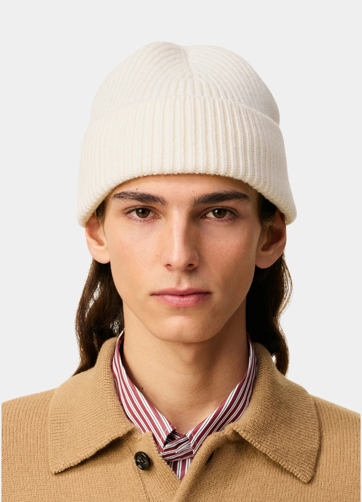 Beige knit beanie with a black heart emblem on a light gray background