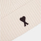 Beige knit beanie with a black heart emblem on a light gray background