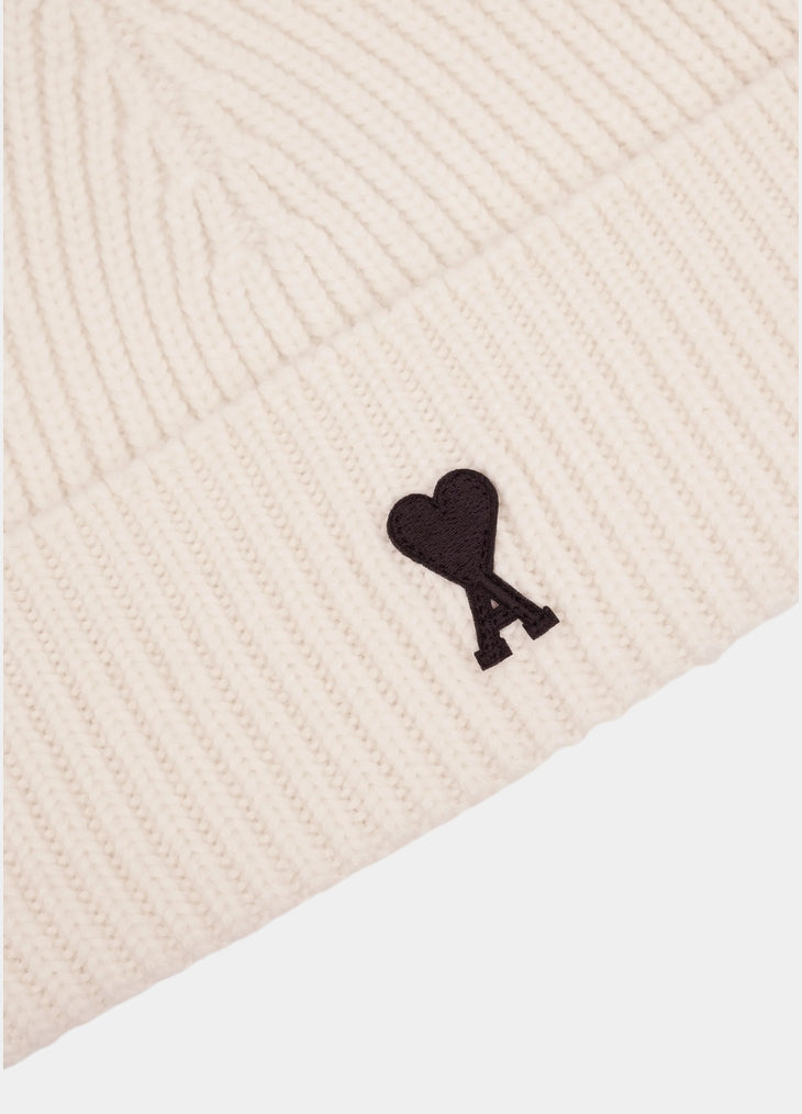 Beige knit beanie with a black heart emblem on a light gray background