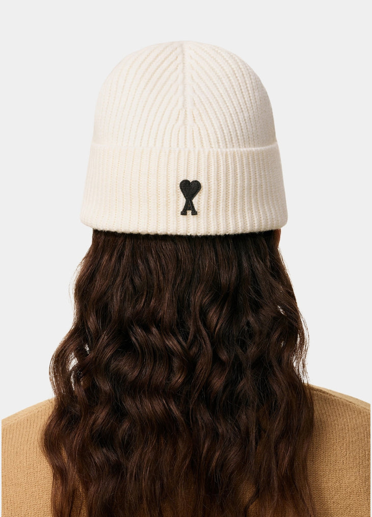 Beige knit beanie with a black heart emblem on a light gray background