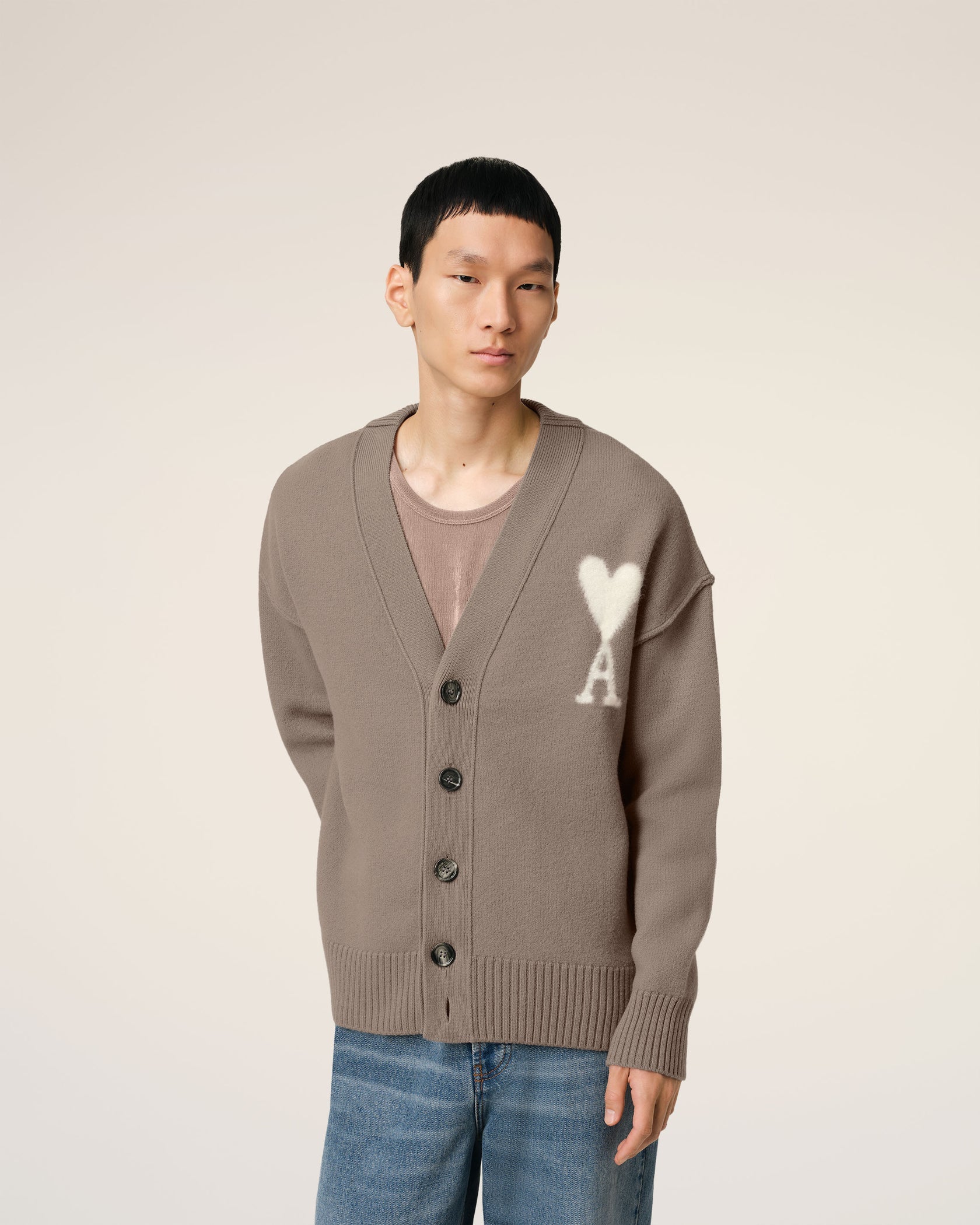 Brown cardigan with a heart and 'AMI' logo on a beige background