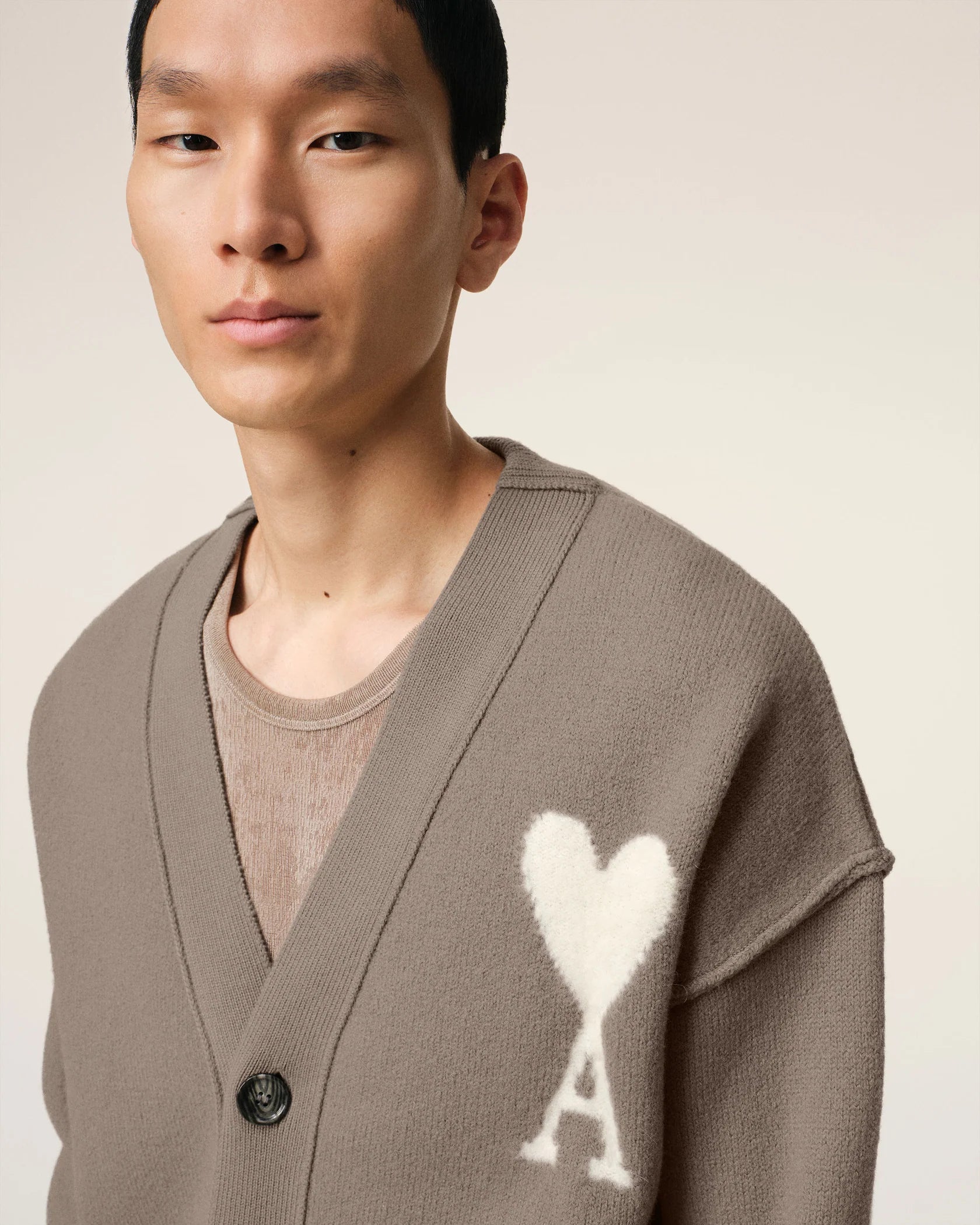 Brown cardigan with a heart and 'AMI' logo on a beige background
