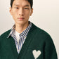 Green cardigan with a heart and 'A' emblem on a beige background
