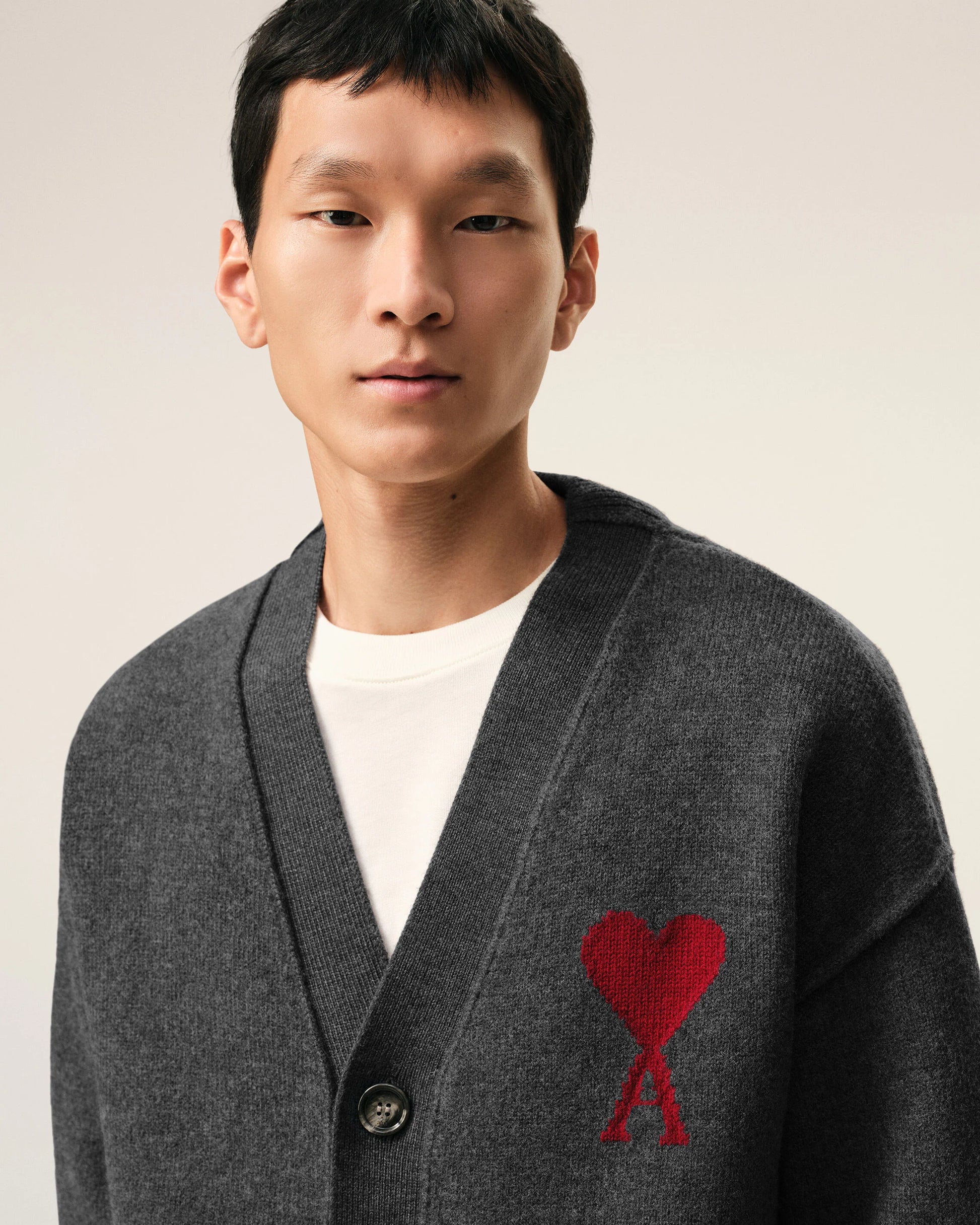 Dark gray cardigan with a red heart emblem on a beige background ami paris
